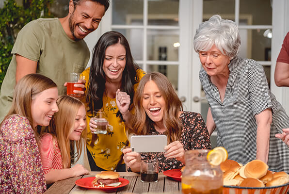Family gathered around a table looking at smartphone laughing together