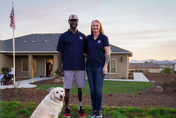 Man with a prosthetic leg stands in front of home with American flag